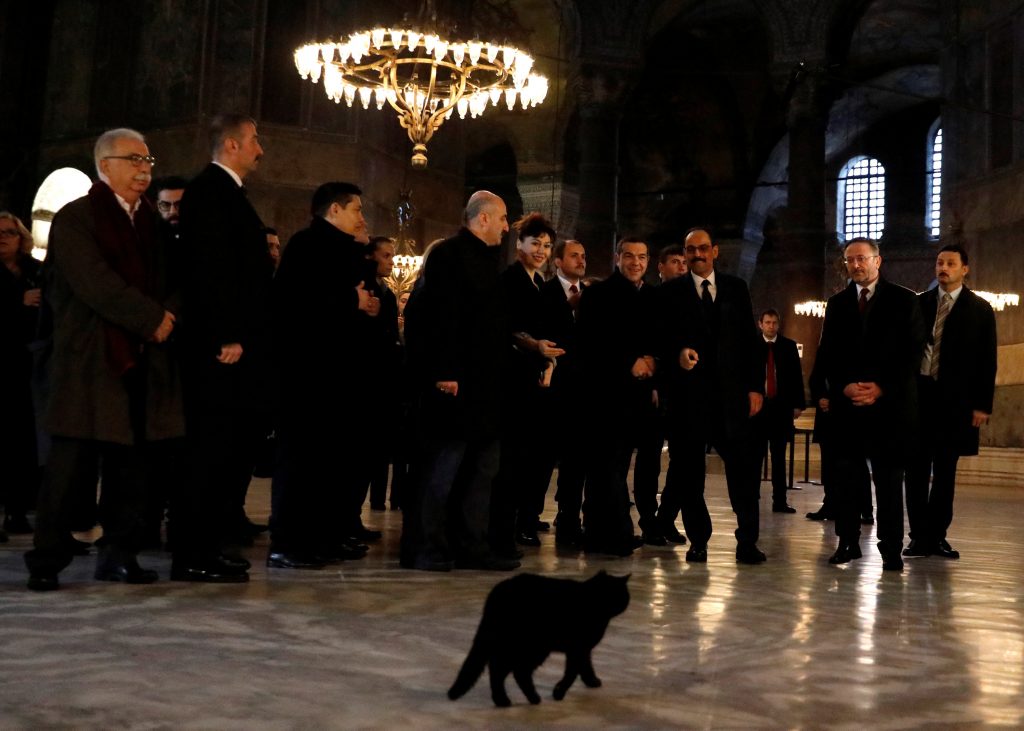 Η ξεναγός και η… «μαυρόγατα» που έκλεψαν τις εντυπώσεις    Τόσο τα τουρκικά όσο και τα ελληνικά ΜΜΕ εντυπωσιάστηκαν τόσο από την παρουσία μιας μαύρης γάτας μέσα στην Αγιά Σοφιά που σουλατσάριζε συνέχεια μπροστά από τον πρωθυπουργό, όσο και από την γοητευτική ξεναγό που υποδέχθηκε και έκανε την περιήγηση στο ζεύγος Τσίπρα – Μπαζιάνα.  Όπως φαίνεται σε φωτογραφίες του πρακτορείου Reuters, η μαύρη γάτα περπάτησε μπροστά από τους επίσημους προσκεκλημένους χωρίς να… πτοείται.  Το περιστατικό φάνηκε να διασκεδάζει ο Αλέξης Τσίπρας, ο οποίος έστρεψε το βλέμμα του προς στη γάτα και άρχισε να γελάει.